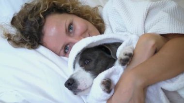 Beyaz Terry bornozlu bir kadın yatakta sevgili köpeğine sarılıyor. Evcil hayvan da rahat beyaz bornoza sarılmış. Sıcak bornozlar içinde sahip ve köpek birlikte atmosfer barışı ve dostluğu yaratır.