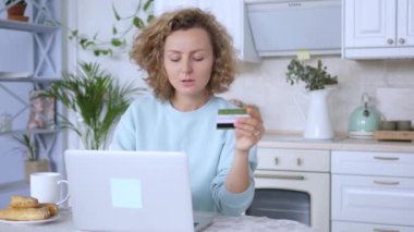 Kadın, online alışveriş için kredi kartı bilgilerini bilgisayara girerek masada oturuyor. Masadaki kadın, online satın alma işlemlerini tamamlamak için kredi kartı bilgilerini dizüstü bilgisayara yazar.