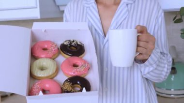 Kadın elinde bir kupa sıcak kahve ve bir kutu lezzetli çörekler taze kahveli çeşitli çörekler tutuyor. Kadın elinde bir fincan kahve ve bir kutu lezzetli çörekler tatlı kahvaltı kahvesi tutuyor.