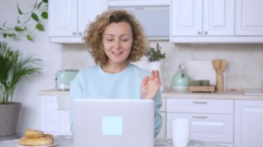 Kadın masada oturmuş arkadaşlarıyla sohbet ediyor. Laptop üzerinden arkadaşlarıyla görüntülü konuşmalar yapıyor. Masa başında oturan kadın, arkadaşlarıyla çevrimiçi laptop konuşmaları kullanarak görüntülü konuşma yapıyor.