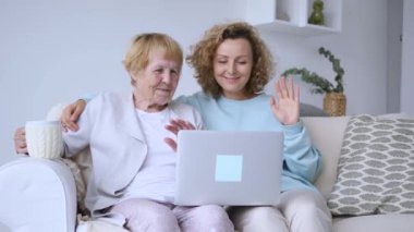 Yetişkin bir kızı olan yaşlı bir anne, kanepeye oturup laptopla sohbet ediyor, olumlu duygular yaşıyor, aile bağı kuruyor. Emekli anne ve yetişkin kız laptopta oturup video izlemenin keyfini çıkarıyorlar.