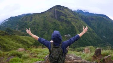 Adam dağın tepesinde otururken kollarını yana doğru açtı. Tırmanma güçlüklerinin üstesinden gelen insan, değer verdiği hedefe ulaştı ve manzarayı seviyor. Görkemli dağlar insana unutulmaz duygular verir.