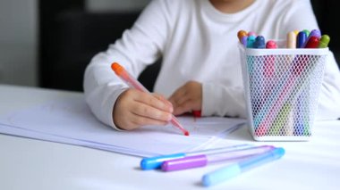 Küçük kız kağıt üzerine keçeli kalemle resim çiziyor. Çocuk özenle çiziyor, parlak bir tablo oluşturuyor. Sanatçı tutkuyla çizer, yaratıcı yetenekler geliştirir. Renkli kalemler fantezileri gerçekleştirir..
