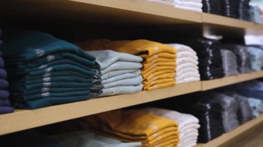 Renkli tişörtler satan bir mağazada rafta düzgünce katlanmış. Mağaza çeşitliliği mankenlerle müşterileri cezbediyor. Mağaza alışveriş ortamı yaratır. Uygun konum ürünleri seçimi kolaylaştırır.