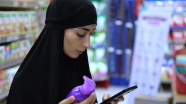 Türbanlı Arap dükkandaki malzemeleri kontrol etmek için telefon kullanıyor. Telefon hızlı bir şekilde bilgi bulmamıza yardımcı olur. Verileri telefonla kontrol ederek, alıcı bilinçli bir seçim yapar. Modern teknoloji alışveriş süreci.