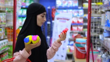 Başörtülü Müslüman kadın alışverişi seviyor, kozmetik ürünleri seçiyor. Alışveriş, mükemmel bakım ürünleri bulmamızı sağlar. Alışveriş süreci geleneklerle modern güzellik eğilimlerini birleştirir. Dikkatli seçim ürünleri.