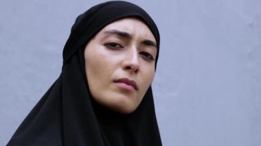 Yakın plan ciddi ve üzgün yüzlü tesettürlü Müslüman kadın. Müslüman derin duyguları bakışlarla ifade eder. Görüntü karmaşıklığı yansıtır Müslüman hayatı. Duygulara ve düşüncelere dikkat çeken etkileyici bir yüz..