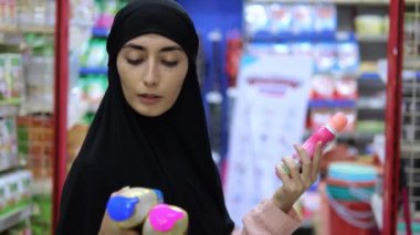 Türbanlı Arap kadın kozmetik ürünlerini dükkanda seçiyor. Kavanozları karşılaştırıyor, kompozisyon kozmetik üzerinde çalışıyor. Çeşitlilik kozmetik ürünleri gereksinimleri karşılayan ürünler bulmamıza olanak sağlar. İlgili ürünlerin seçimine yaklaş.