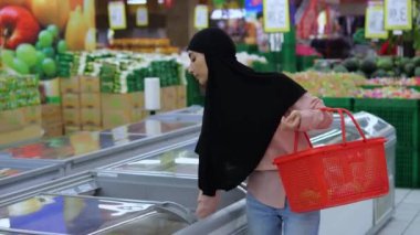 Doğulu tesettürlü kadın süpermarketteki buzdolabından donmuş yiyecek seçiyor. Alıcı buzdolabını açarken malları dikkatlice inceler. Buzdolabından aldıklarıyla el sepeti tutan bir kadın.. 
