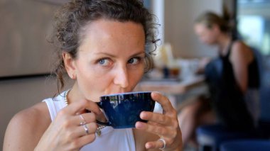 Kentsel kahve dükkanında genç profesyonel cappuccino, sakin bir rahatlama anını ve kişisel zevkini vurgulayan yumuşak doğal ışıklandırma. Her gün kahve tüketimi kavramı.