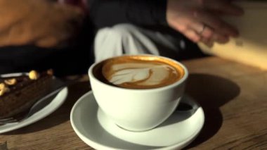 Gün ışığı, ahşap kafenin içini hafifçe aydınlatan, kremalı kapuçinonun tadını çıkaran bir kadın ve dinlendirici öğle arası sırasında çikolatalı pasta dilimi. Bir fincan cappuccino için kafe sıcak atmosfer