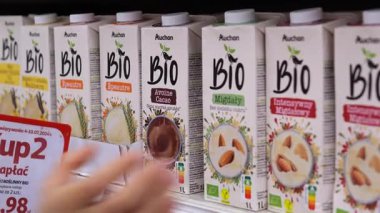 Varşova, Polonya - 01 Mayıs 2024: Müşteri eli çoklu lezzet ve tanıtım tabelalarını süpermarket raf ekranında tararken organik bitkisel süte doğru uzanan müşteri eli