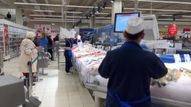 Varşova, Polonya - 01 Mayıs 2024: Dondurulmuş balık tezgahında müşteriye servis yapan mavi önlük giyen profesyonel balıkçı, ezilmiş buzun üzerinde dikkatlice taze deniz ürünleri tartıyor.