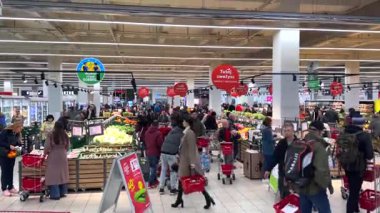 Varşova, Polonya - 01 Mayıs 2024: Alışveriş arabaları ile çok sayıda müşteri hareketli bir süpermarkette geziniyor, iyi stoklanmış raflardan ve soğutulmuş vitrinlerden taze ürünler ve diğer ürünleri seçiyorlar