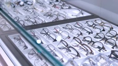 Birden fazla gözlük, müşterilerin bakmaları ve seçmeleri için çeşitli çerçeve biçimleri ve renkleri gösteren parlak cam bir vitrin içinde düzgün bir şekilde düzenlenmiştir.