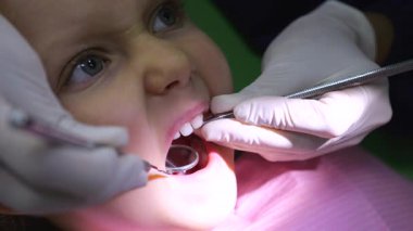 Profesyonel pediatri dişçisi koruyucu eldiven takıyor. Genç hastaların dişlerini dikkatlice inceliyor. Klinik ortamdaki oral sağlık kontrolü sırasında diş aynası kullanıyor ve muayene ediyor.