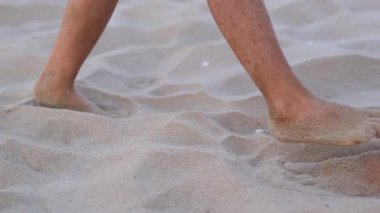 Yalın ayaklı çocuk yaz tatili boyunca yürüyüş rehberliği edinerek yumuşak kumsalda yetişkin ayak izlerine dikkatlice basıyor.