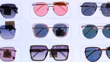 Çeşitli çerçeve şekilleri ve lens renklerine sahip birden fazla güneş gözlüğü beyaz bir duvara yerleştirilerek görsel olarak çekici ve düzenli bir sunum oluşturulmuştur. Mağazada güneş kremi konsepti