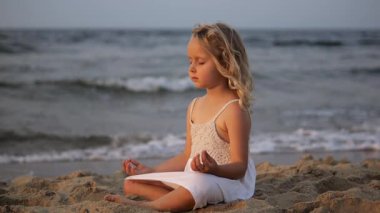 Altın güneş ışığı, sakin genç bir kızı kumlu bir plajda meditasyon yaparken aydınlatıyor. Yumuşak dalgalar, huzurlu tefekkür için sakin bir zemin sağlıyor.