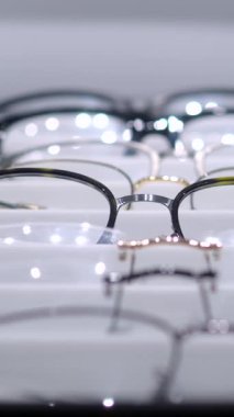 Dikey ekran, çoklu gözlük düzgün bir şekilde düzenlenir ve parlak beyaz bir rafta gösterilir, müşterilerin bir optik mağazada gezip seçmeleri için çeşitli stiller ve tasarımlar sergilenir