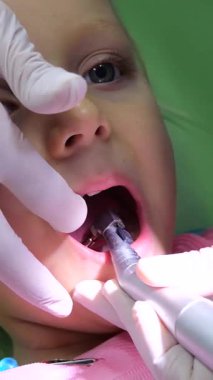 Dikey ekran, pediatrik diş hekimi elektronik aletle çocuğun dişlerini dikkatle inceliyor, modern klinik ortamda oral sağlık kontrolü yapıyor.