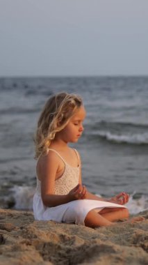 Dikey ekran, plajda yoga ve meditasyon yapan barışçıl bir çocuk, güzel bir gün batımında okyanusta iç huzuru ve farkındalığı buluyor.