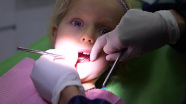 Pediatrik dişçi koruyucu eldiven takıyor. Genç kızların dişlerini dikkatlice inceliyor. Modern diş sağlığı kliniğinde rutin kontroller sırasında diş aynası ve sonda kullanıyor.