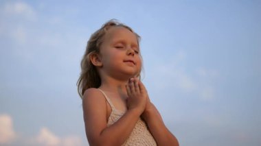 Manevi olarak meditasyon yapan genç bir kız ellerini sıkar ve gözlerini açık havada barışçıl bir şekilde kapatır. Geniş mavi gökyüzü arka planına karşı iç huzuru yayar. Çocukluktan beri Tanrı 'ya dua etme kavramı