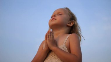 Genç kız elleri dua ederken, gözleri kapalı, masmavi bir gökyüzünün altında duruyor. Huzur ve masumiyet anı yakalıyorum. Çocukluktan beri Tanrı 'ya inanç kavramı