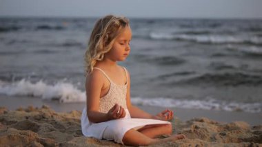 Gün batımında plajda yoga ve meditasyon yapan huzurlu bir çocuk dalgaların arasında iç huzuru ve farkındalığı buluyor.