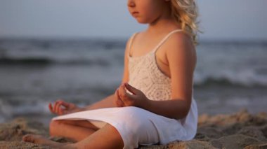 Altın saat boyunca farkındalığı somutlaştıran, ritmik okyanus dalgalarının yanında huzurlu meditasyon yapan, dinginliği ve içsel sakinliği nazikçe yoga pozuyla yaşayan genç bir kız.