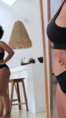 Dikey ekran, kendine güveni olan Afrikalı Amerikalı kadın siyah iç çamaşırı giyip vücudunu olumlu bir şekilde değerlendiriyor.