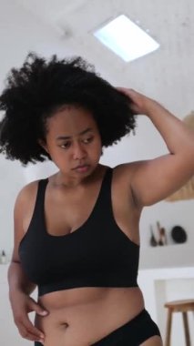 Dikey ekran, güzel ve iri yarı Afro-Amerikan kadın göbeğini ve kolunu inceliyor, kilosu ve vücudu hakkında endişeli, iç çamaşırlarıyla parlak bir odada duruyor.