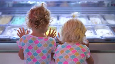 Dondurma vitrininde dikilmiş renkli tatları heyecanla inceleyen ve dondurulmuş lezzetli bir ziyafet çekme beklentisiyle bekleyen iki kız kardeş.