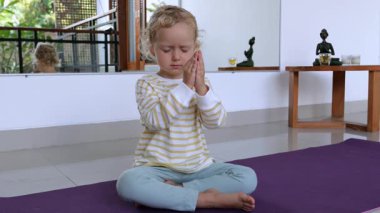 Mor yoga minderi üzerinde meditasyon yapan genç sarışın bir kız. Huzurlu ev ortamında farkındalık ve iç huzuru, sağlığın ve duygusal dengenin somutlaştırılması.