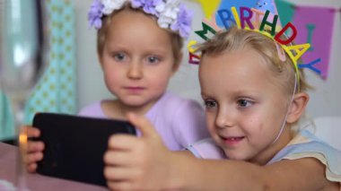 Genç kız kardeşler neşeli doğum günü şapkaları takarak neşeli anları yakalıyorlar, neşeli ev kutlamalarında renkli dekorasyonlar yaparak akıllı telefon özçekimleri yapıyorlar.