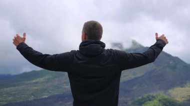 Genç erkek turist, Bali, Endonezya 'da aktif bir volkan olan Batur Dağı' nın manzarasının keyfini çıkararak özgürlüğünü ve merakını ifade ediyor.