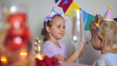 Parti şapkası takan iki genç arkadaşla neşeli bir çocukluk anıydı. Doğum günü kutlaması sırasında kaynaşıyor, makyaj yapıyor ve süslü masalarda neşeli deneyimleri paylaşıyordu.