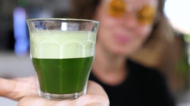 Buğday çimeni. Gülümseyen kadın beslenme uzmanı canlı yeşil meyve suyu sunuyor, sağlıklı olduğunu ve el değmemiş beyaz arka planda detoks yaptırdığını gösteriyor. Sağlıklı yaşam tarzı kavramı