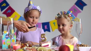 Sevgi dolu anne pastada beş doğum günü mumunu dikkatle yakarken aynı zamanda aile evinde ikiz kız çocuklarının dönüm noktasını kutluyor.