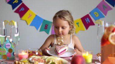Sevimli küçük kız beşinci doğum gününü kutluyor. Renkli bir pasta dilimine bakıyorum. Üzerinde beş numaralı altın mum ve meyveli bir mum var. Mumlar. Ve mutlu yıllar bayrağı