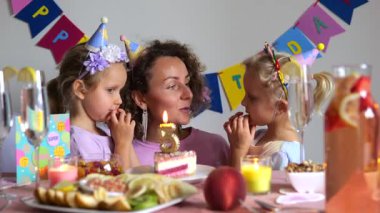 Mutlu bir aile doğum günü kutlaması, beşinci doğum günü partilerinde annelerini öpen ve kucaklayan iki ikiz kız çocuğu, pasta, mum, meyve ve süslemelerle