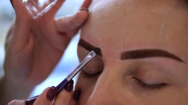 Güzellik uzmanlarının ellerine dikkatlice bir müşterinin yüzüne kaş makyajı uygulayıp doğal özelliklerini hassasiyet ve beceriyle arttırıyorlar. güzellik endüstrisi konsepti