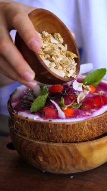 Dikey ekran canlı pembe smoothie kasesi ahşap kapta, katmanlı taze meyve, fındık ve gevrek granola, renkli gurme kahvaltı hazırlama ve tropikal malzemeler.