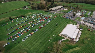 Kırsal kesimin ortasındaki bir otoparkta sıra sıra bekleyen geniş bir grup arabanın görüntüsü.