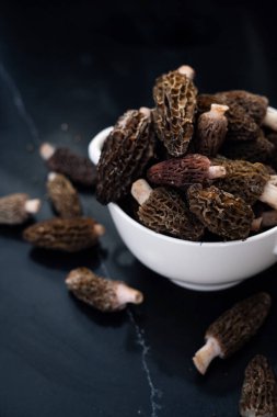 Siyah arka planda beyaz bir kasede gurme mantarları yakın plan. Bu hassas mantarlar, zengin, topraksı lezzetleri ve eşsiz dokuları için mutfak yemeklerinde çok değerlidir.