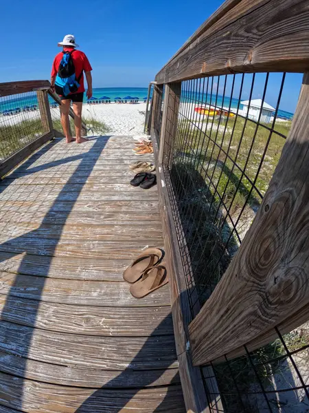 A man walking along a wooden path to the beach at Rosemary Beach, Florida on a sunny summer day.