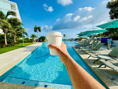 Nassau, Bahamalar - 1 Haziran 2024: Bahamalar 'ın başkenti Nassau' daki The Royal Bahamian Sandals Resort 'ta havuz kenarında kahve tutan bir el.