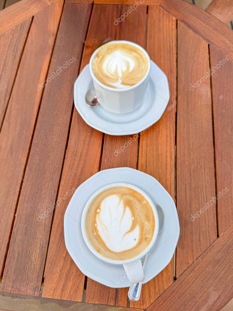 Two delicous coffee latte with a foam leaf in the MSC Seashore Cruise Ship Yacht Club outdoor lounge on a wooden table.