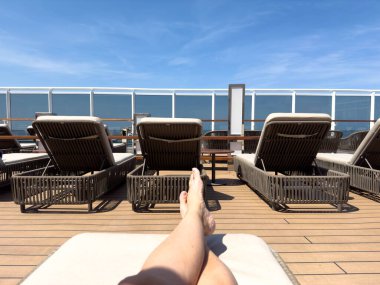 Güneşli bir günde okyanusa bakan bir yolcu gemisinde şezlongda oturan biri..